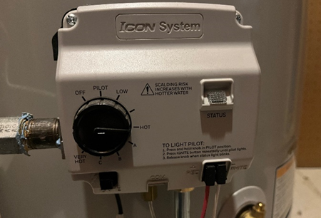 Close-up of an ICON System water heater control panel, featuring a temperature adjustment dial, status indicator, and pilot light instructions. Various wires and gas connections are visible, emphasizing the unit's operational components.