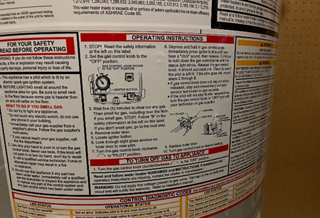 Close-up of a water heater instruction label displaying safety warnings, operating instructions, and diagnostic codes. The label includes step-by-step guidance for lighting the pilot, turning off the gas, and troubleshooting system issues.