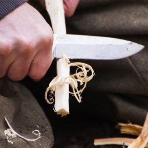 Survivalist making feather sticks from a piece of pinewood with a bushcraft knife
