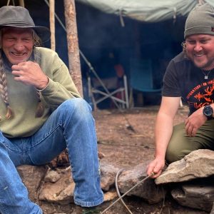 Two survivalists laugh around a cooking fire at survival class