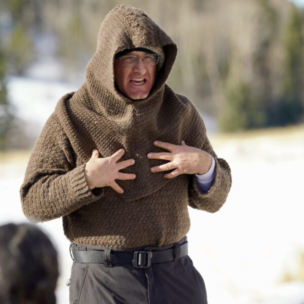 Instructor in a brown wool hooded sweater teaching an outdoor winter class with snow and trees in the background
