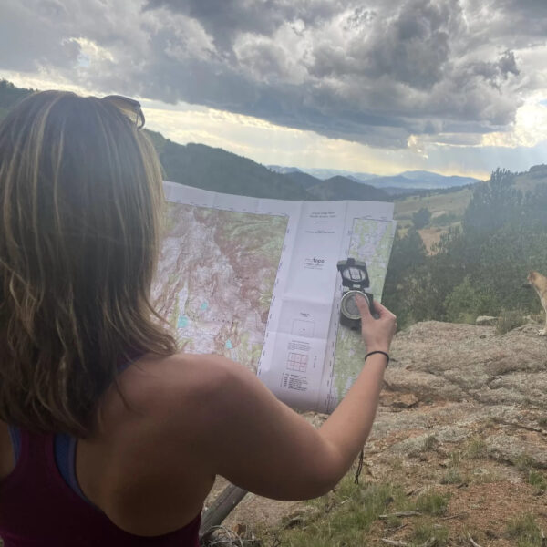 A woman holds a compass and map, navigating from a rocky overlook under a stormy sky