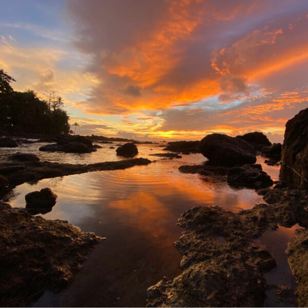 Fiery orange and pink sunset over a rocky tropical shoreline in Costa Rica, with reflections of the sky shimmering in the tide pools.