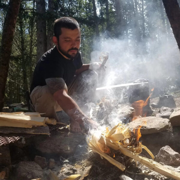 Man starting a fire with wood shavings during a wilderness survival course in a forest setting