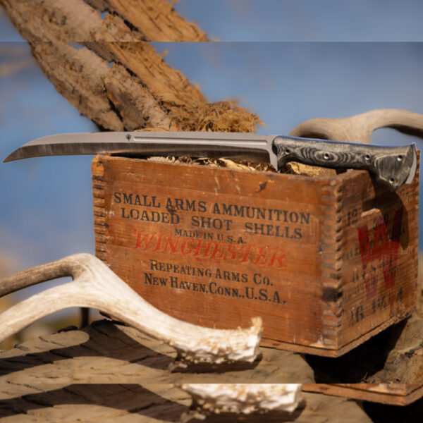 The Gallantry knife resting on top of a weathered Winchester ammunition box, with antlers and natural elements surrounding the setup against a blurred outdoor backdrop.