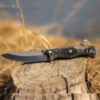 Fixed-blade survival knife with a black textured handle and matte blade resting on a weathered tree stump in a dry, grassy outdoor setting.