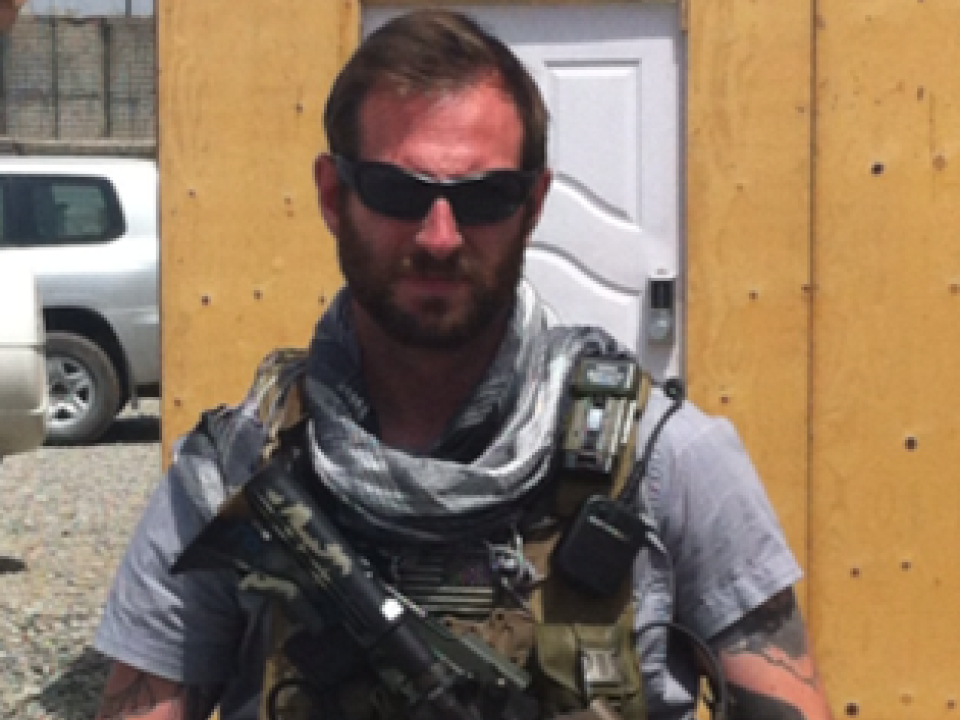 Chris, veteran with 21 years of military service, wearing tactical gear and sunglasses in a training environment.