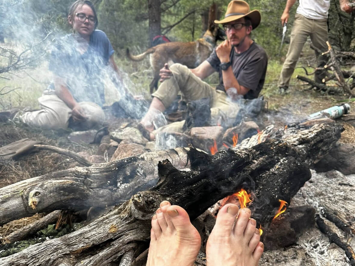 Students relaxing around a campfire during The Survival University’s 26-Day Advanced Immersion Course in Colorado, reflecting on training and life in the wilderness.