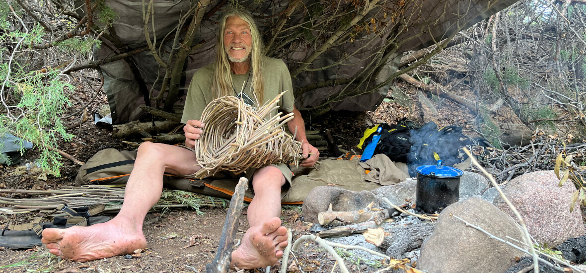 Student practicing bushcraft in a primitive shelter during a wilderness course in Colorado, learning fire and weaving skills.
