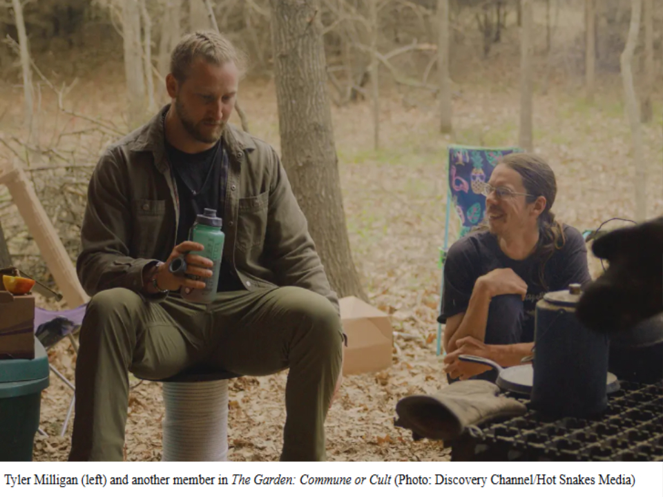 Tyler Milligan sitting outdoors during filming of The Garden: Commune or Cult, holding a water bottle while another cast member smiles beside him at a woodland campsite.