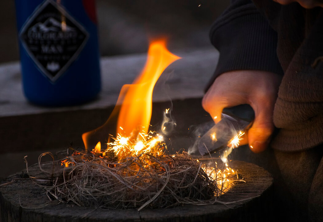 Student learning fire-starting with a ferro rod during a wilderness survival course in Colorado.
