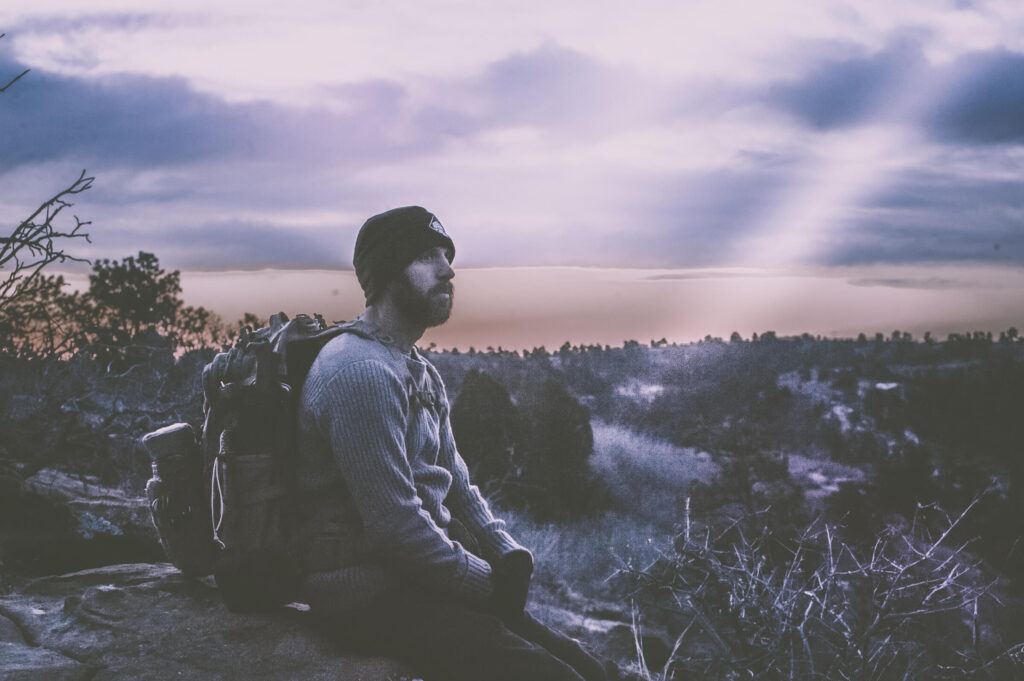 Jason Marsteiner sitting on a rocky ridge at dusk, reflecting on awareness, resilience, and the fragility of modern comfort.