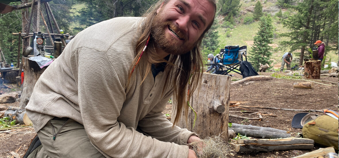 Student smiling while practicing fire-starting skills during a survival training course in the Colorado mountains.
