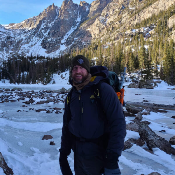 Jason Marsteiner standing near a frozen alpine creek on a clear winter day, illustrating how cold environments can feel safe while still impairing judgment