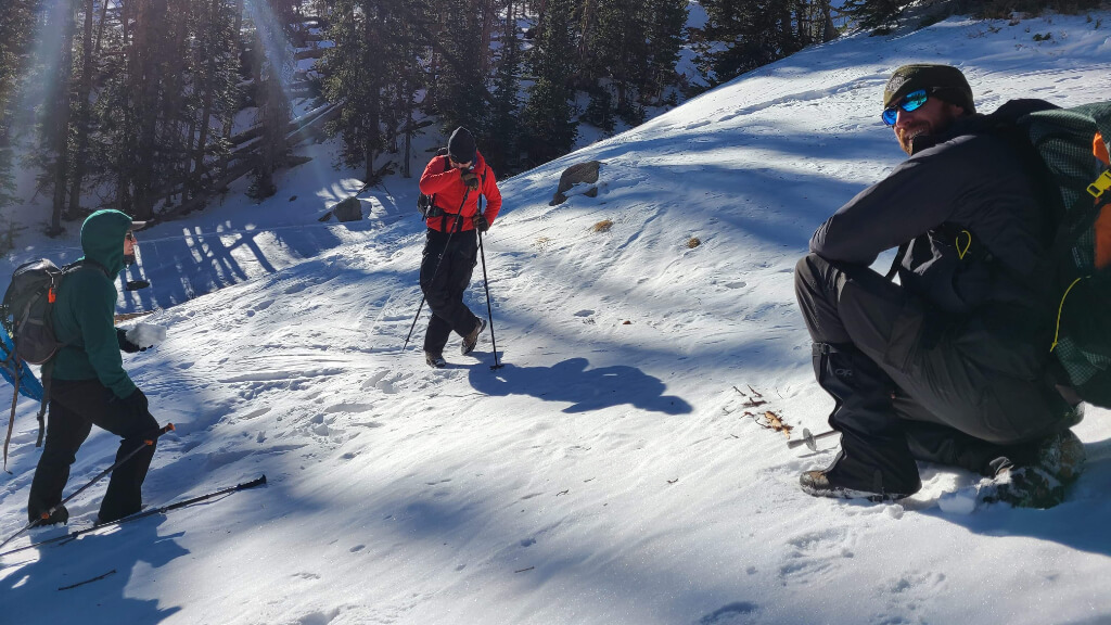 Instructor kneeling in deep snow while digging an avalanche test pit during winter backcountry training
