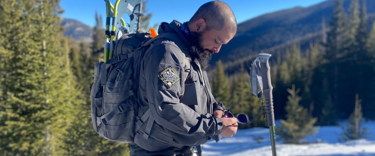 Man adjusting clothing layers in snowy backcountry while managing temperature during winter travel