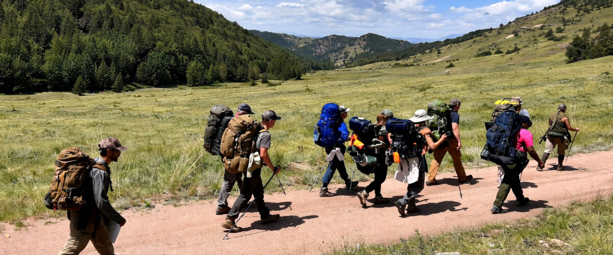 Hikers walking along a wide, well maintained trail in open terrain under clear skies, representing typical hiking conditions.