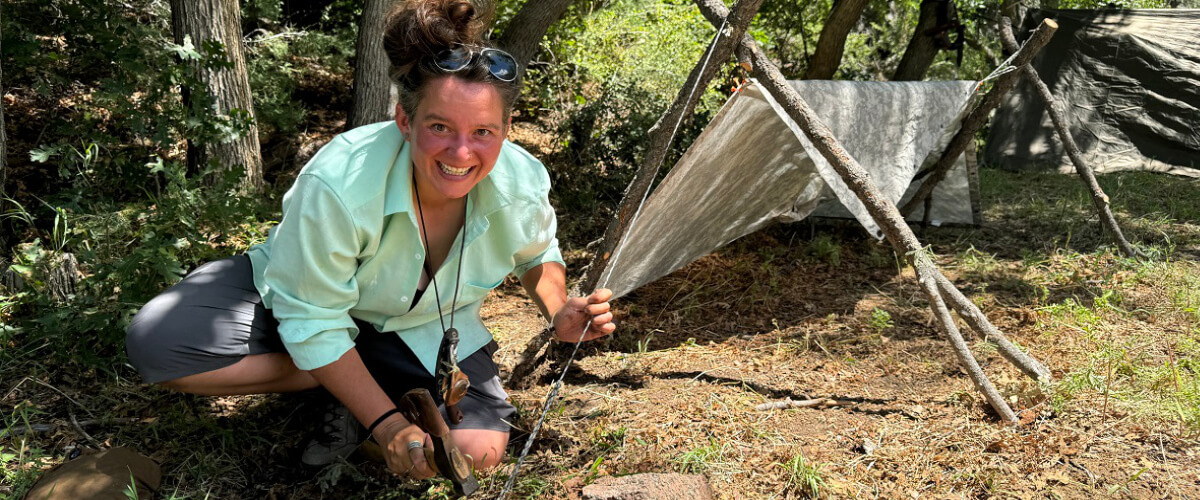 Solo traveler setting up a simple shelter in forested terrain as a preventative decision rather than a reaction to crisis