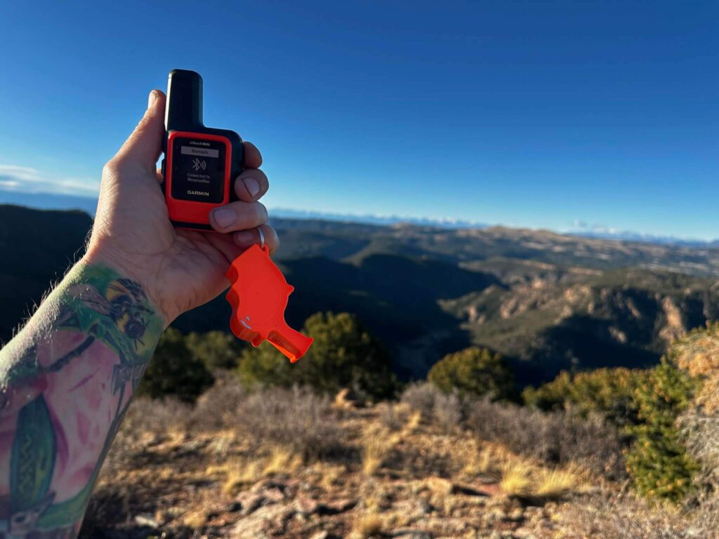 Hand holding a satellite communication device overlooking mountain terrain as part of trip planning and lost proof preparation