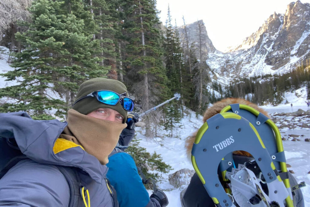 Small group of winter hikers paused below a mountain cirque, carrying snowshoes and looking toward steep snow covered terrain near the summit.