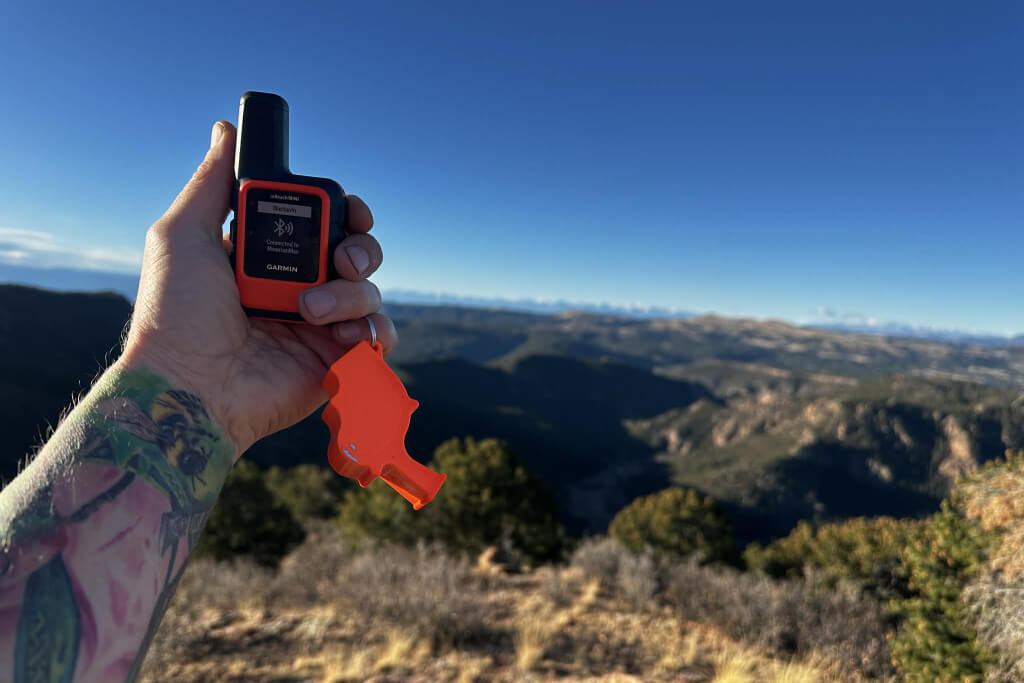hand holding garmin inreach mini satellite communicator in remote mountain terrain for emergency signaling