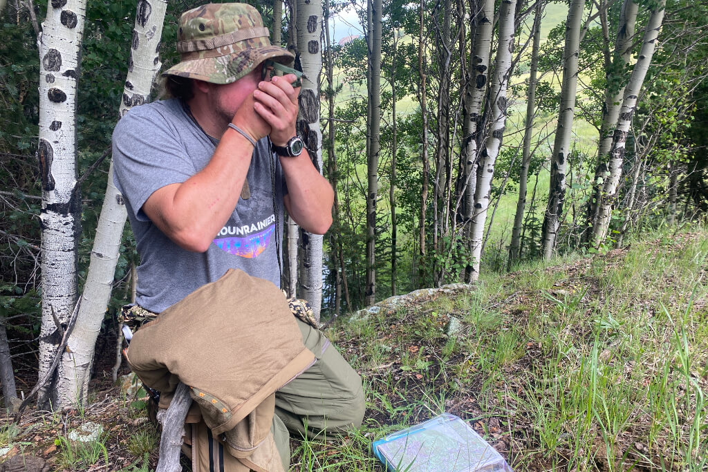 Hiker kneeling in the forest shooting an azimuth with a compass while navigating with a map