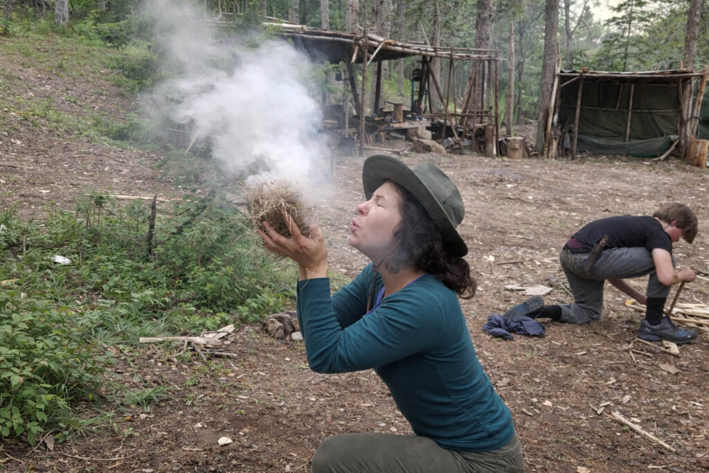 Student blowing into tinder bundle while practicing primitive fire starting during survival training