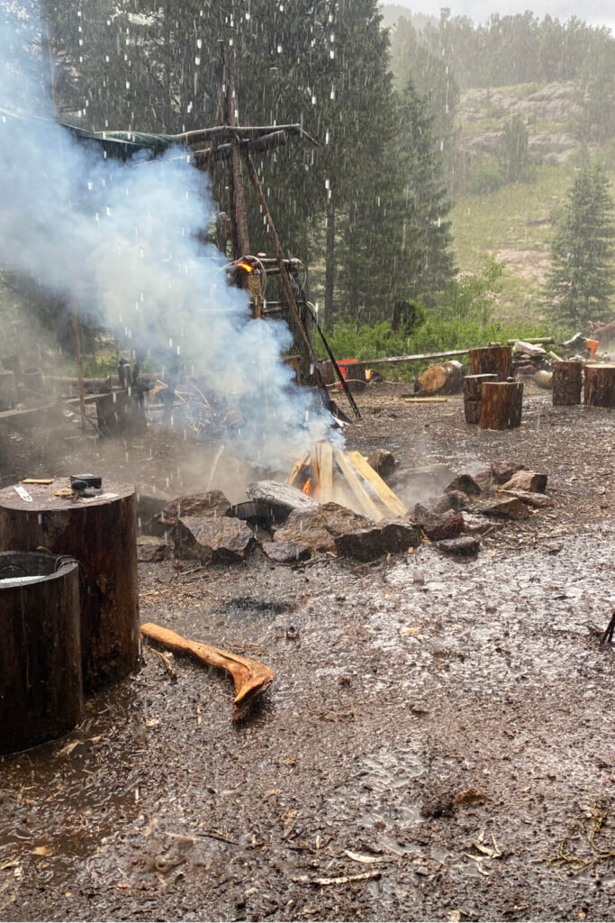 Wilderness survival training camp with fire burning during heavy rain and muddy ground conditions