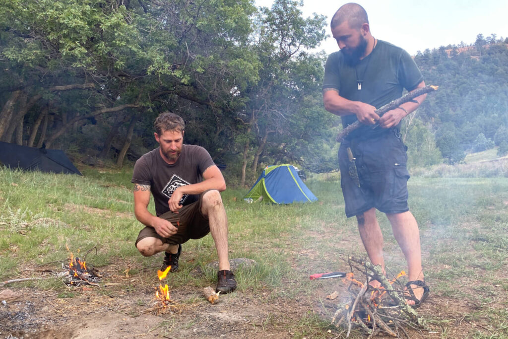 Two wilderness instructors testing fire starting techniques in wet outdoor conditions