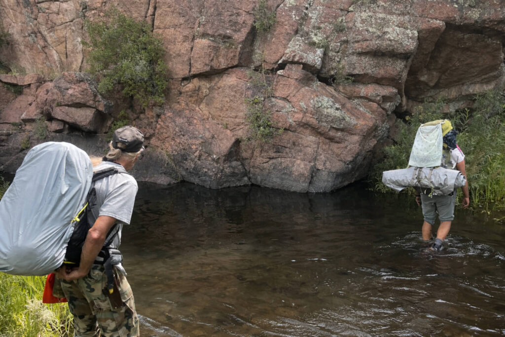 Backpackers crossing mountain stream during wilderness leadership and situational awareness training