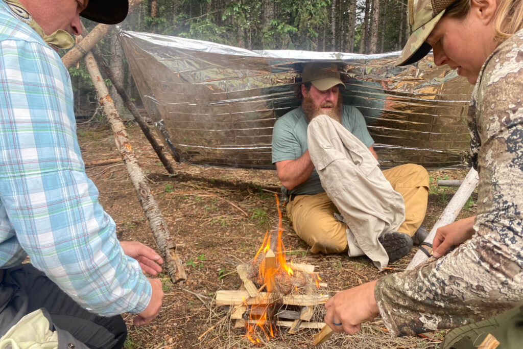 Students building fire under emergency shelter during cold weather wilderness survival training