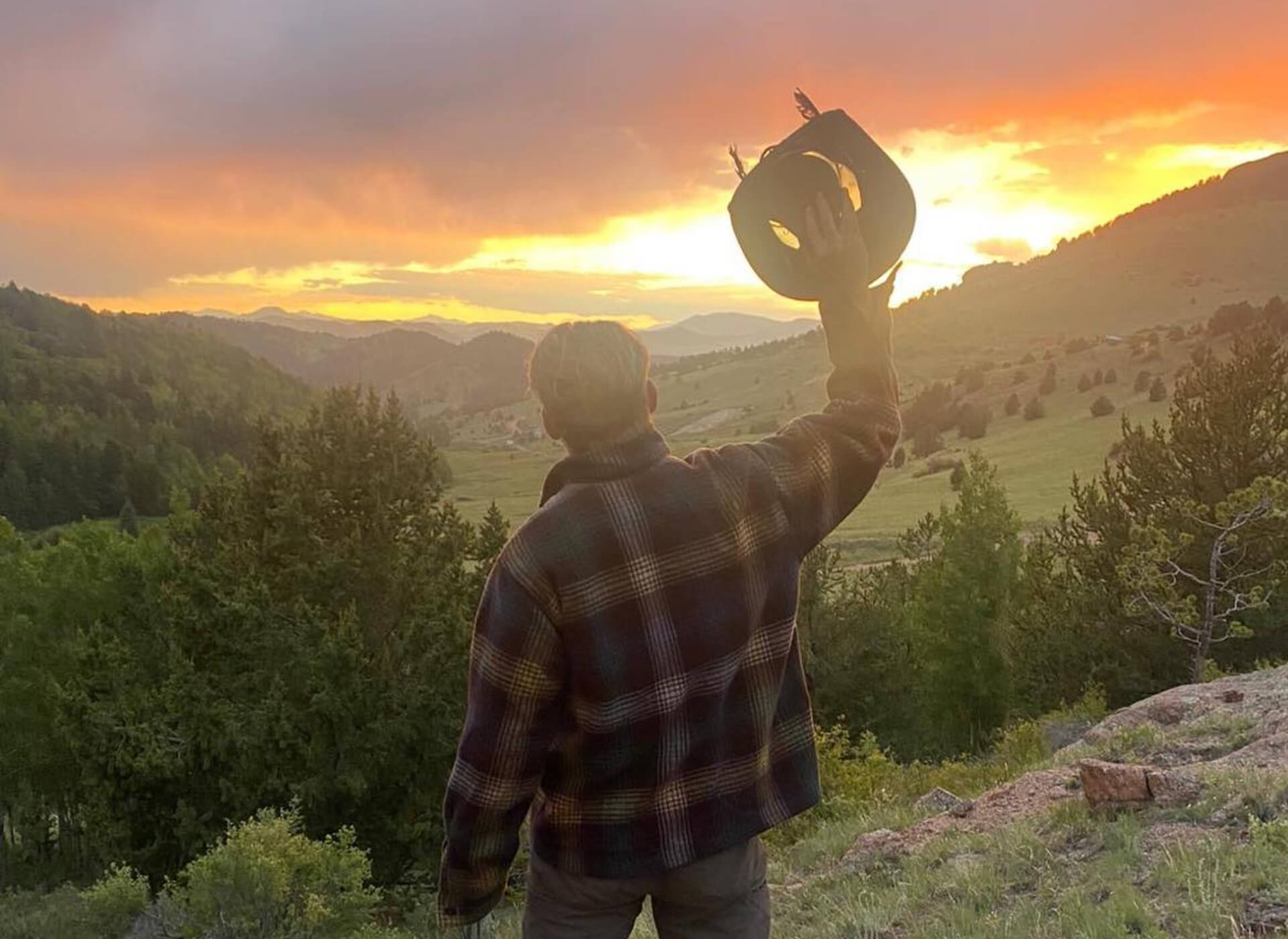 A person raises a hat while overlooking Colorado mountain country at sunset