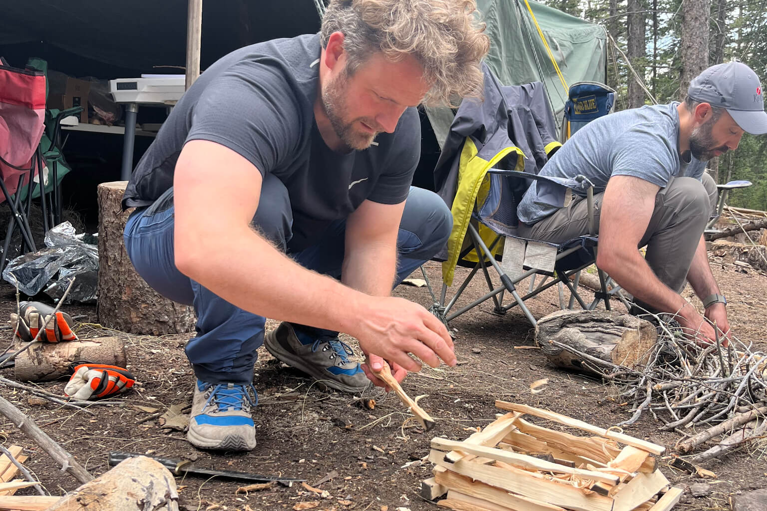 Two participants building a fire using small sticks during outdoor survival and leadership training