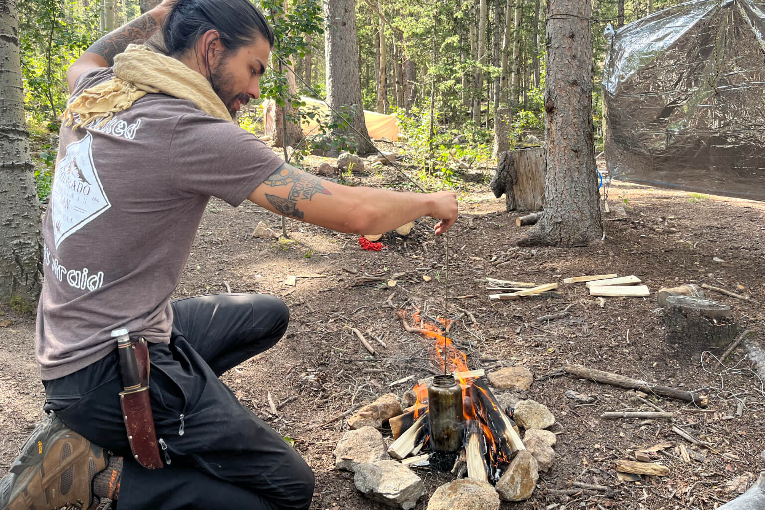 A student practices boiling water in a metal container over a field fire