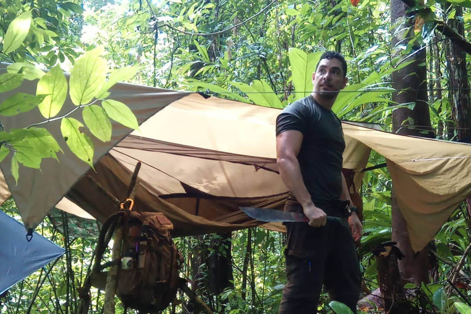 Albert Lopez standing in a jungle shelter camp in Costa Rica holding a machete during Jungle Brotherhood training