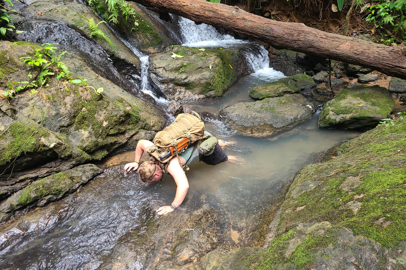 Man with backpack drinking from a jungle stream in Costa Rica during training