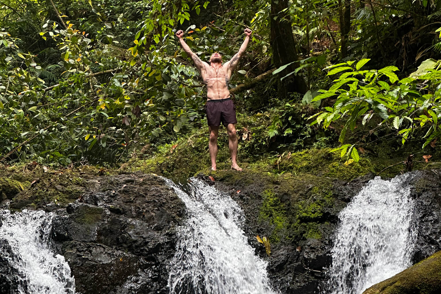 Man standing on a jungle waterfall with arms raised in Costa Rica
