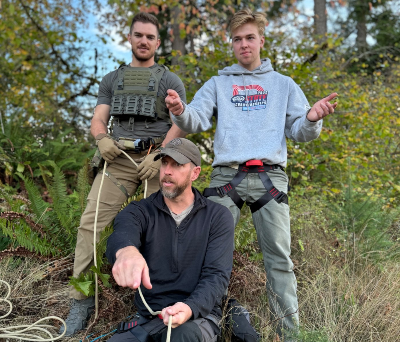 Jason Marsteiner pointing during outdoor rope training with two participants wearing harnesses