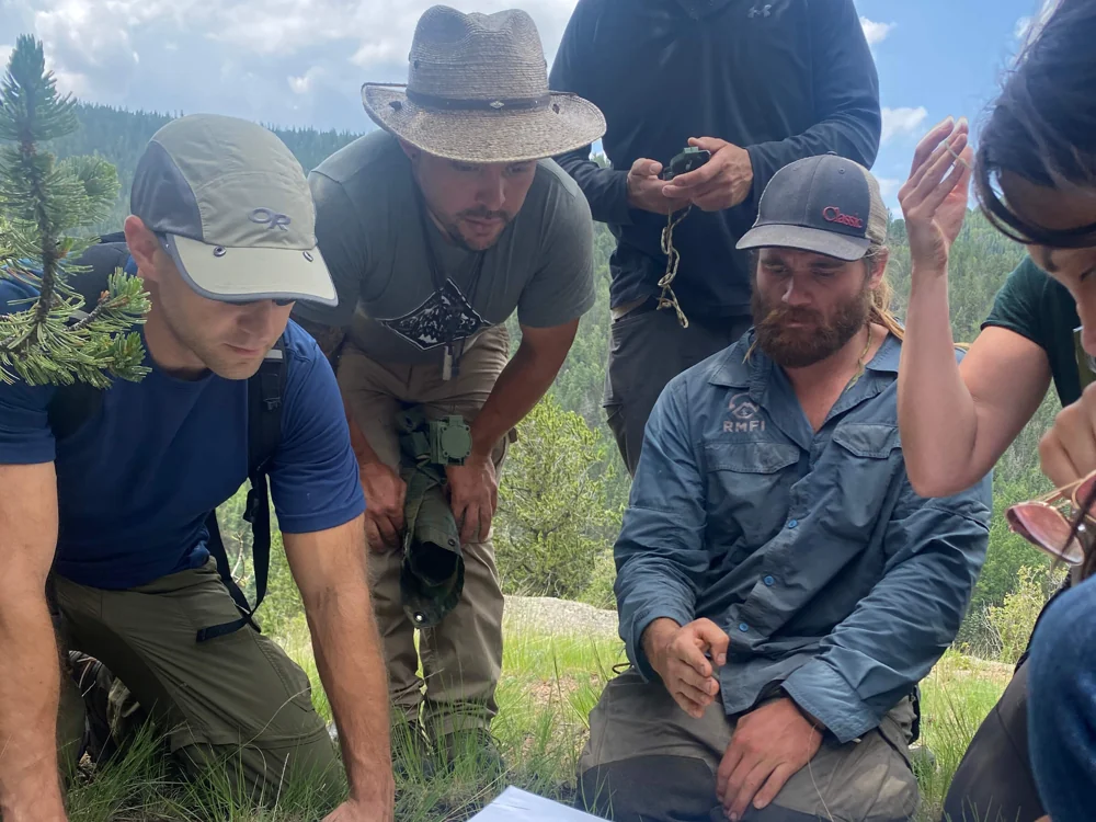 Group gathered around a map during field navigation training in the Colorado mountains.